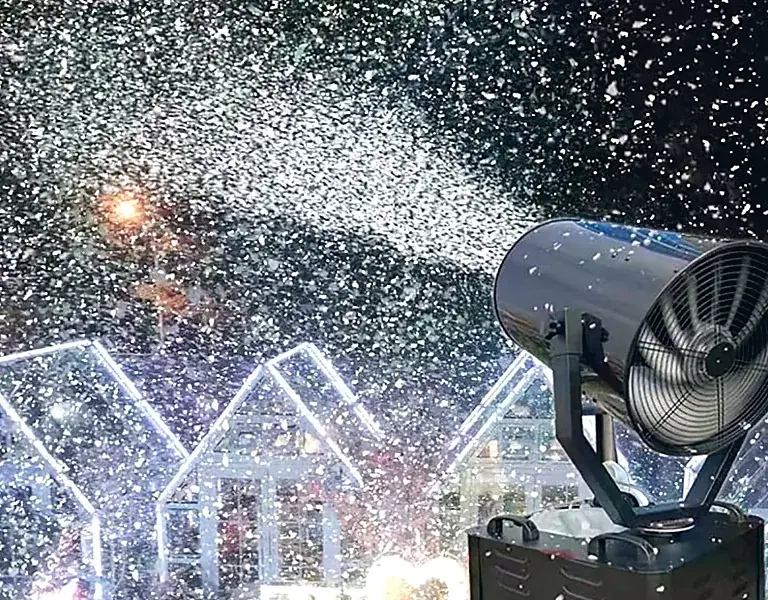 Máquina de nieve artificial lanzando copos sobre casetas iluminadas de un mercado navideño